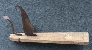 Uprightly standing knife which is used on the ground and kept in place by the foot. The tool to the left is used when peeling the inside fruit of a dried coconut.